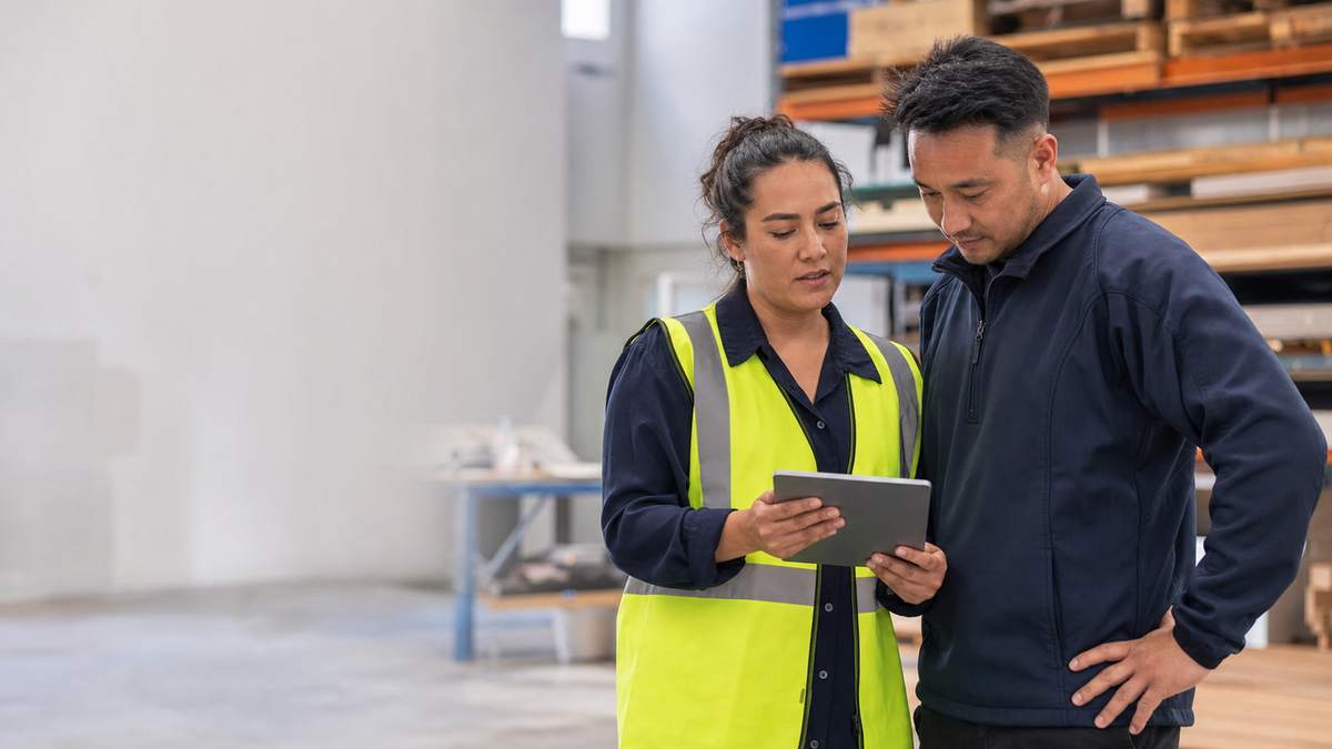 A supervisor in a hi-vis vest and a colleague reviewing training on a tablet in a New Zealand warehouse