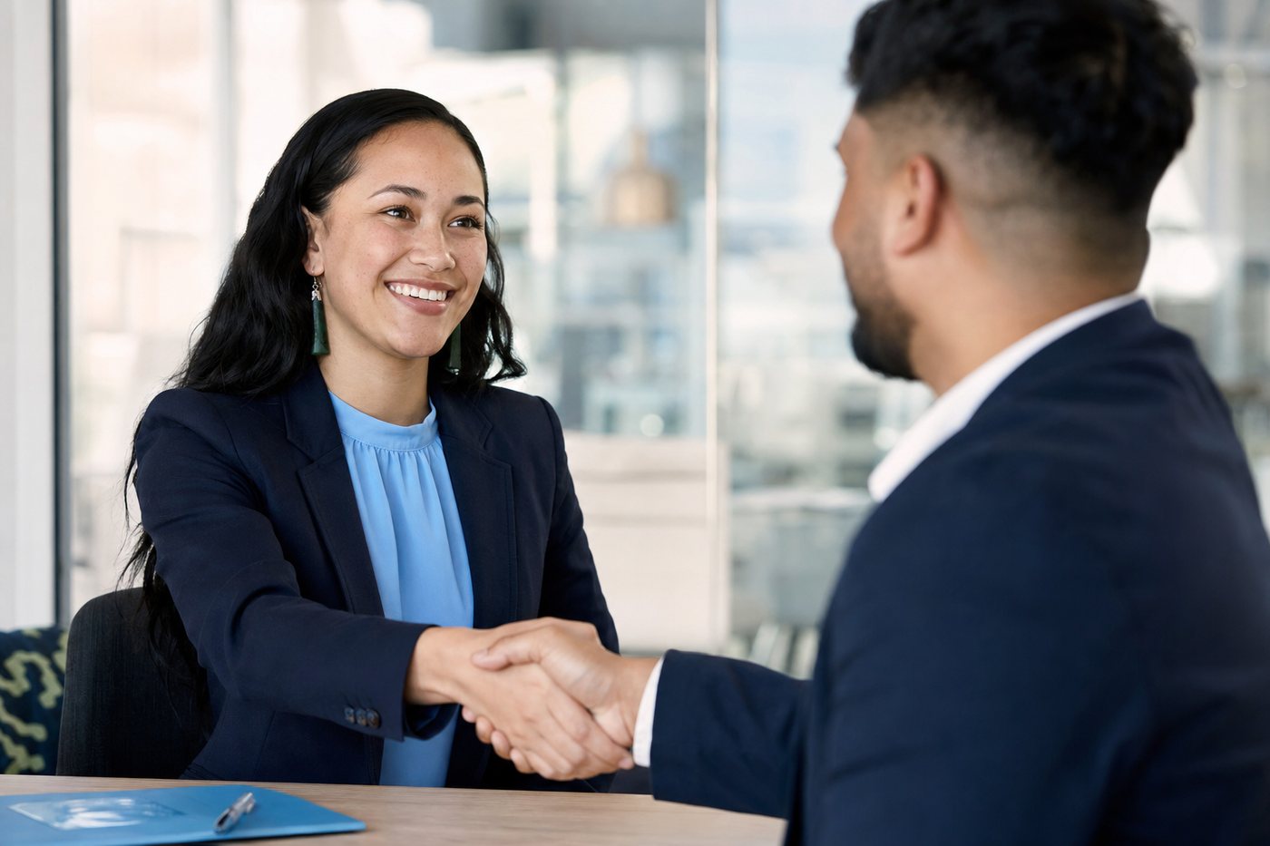 Two people shaking hands across a table at the start of a job interview